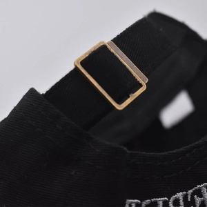 Close-up of the adjustable bronze metal buckle and cotton strap on the black baseball cap