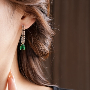 Detail of a gold teardrop earring with green zircon stone worn by a model