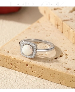 Detail of square halo opal ring with white pave stones on natural stone backdrop