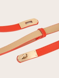 Close-up of orange slim leather belt showing cross pattern and golden metal turn-lock buckle