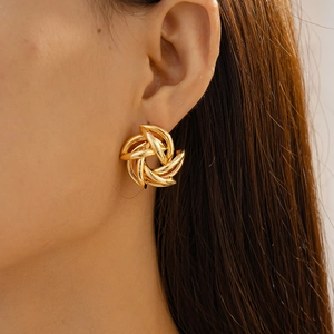 Macro shot of gold geometric spiral flower stud earrings worn on a model's ear