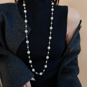 Close-up of elegant long pearl necklace worn over a black sweater for a stylish look