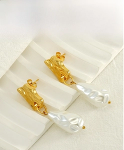 Macro detail of irregular baroque pearls and hammered gold metal studs on a white display