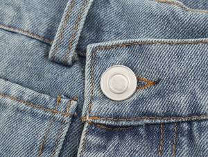 Detailed macro of silver metal button and orange stitching on blue denim fabric