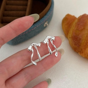Detail shot of silver ribbon bow stud earrings held on fingertips in a lifestyle setting