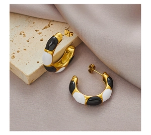 Close-up of gold-plated C-shaped enamel earrings on stone and silk background