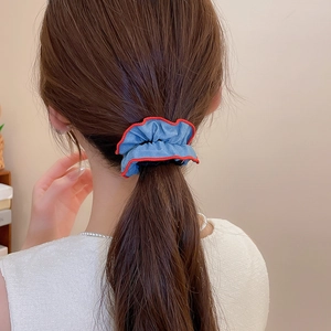 Detail shot of a denim blue scrunchie with red edges worn on a low ponytail hair style