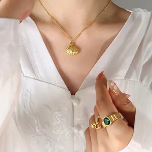 Fashionable gold shell pendant necklace and green gemstone ring set on a model