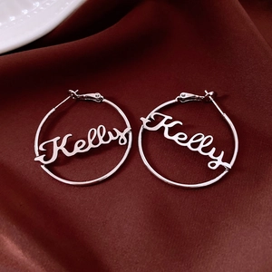 Detail of silver hoop earrings with hollow Kelly name design on dark red silk