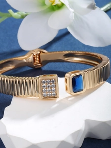 Detailed close-up of a gold textured open bracelet featuring a blue square gemstone and zircon