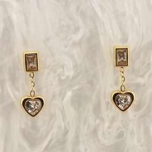Detailed macro view of 18K gold plated heart zircon earrings on white soft plush surface