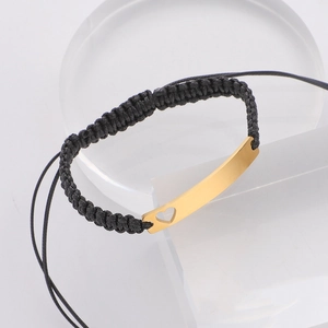 Detail of black woven rope bracelet featuring a gold curved bar with hollow heart cutout