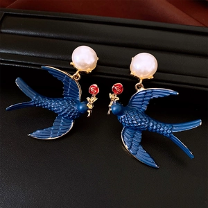 Detail of vintage enamel swallow earrings with red rose and pearl drop on black background