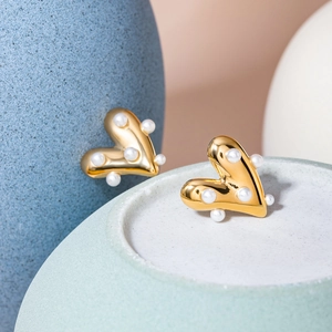 Detailed close-up of 18k gold heart earrings with white pearls on a ceramic dish