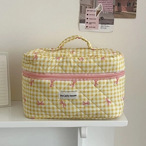 Detail view of quilted yellow plaid makeup bag with pink bow and handle on shelf
