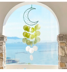 Detail of moon-shaped shell wind chime hanging in front of a scenic ocean view window