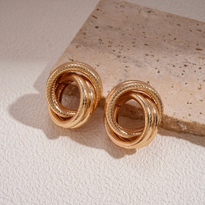 Macro shot of gold twisted rope geometric earrings on a minimalist stone base