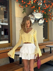 Pale yellow V-neck hollow knit cardigan with flared sleeves and white tiered mini skirt