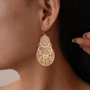 Vue détaillée de boucles d'oreilles dorées ajourées portées par un mannequin en gros plan