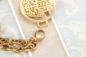 Macro detail of golden Hamsa Hand charm and double-layered stainless steel chain link
