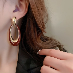 Detailed close-up of a model wearing retro oval enamel drop earrings in burgundy and gold