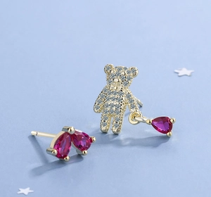 Detail of asymmetrical bear earrings with pink heart stones on blue background