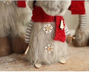 Close-up of grey plush Christmas reindeer with red scarf and wooden ski accessories