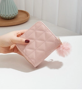 Detailed view of pink quilted wallet with zipper and fluffy pompom keychain charm