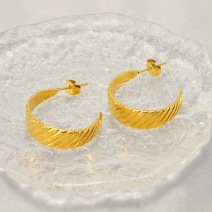 Fashionable gold stainless steel twisted hoop earrings displayed on a glass tray