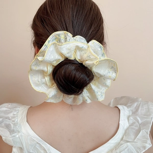 Detail of floral chiffon scrunchie with yellow scalloped edges on a hair bun