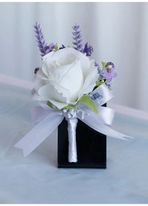Detail of white rose boutonniere with lavender accents and light purple ribbon bow