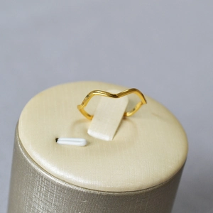 Close-up of minimalist gold-plated wavy ring displayed on a cylindrical stand