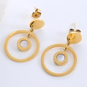 Close-up of golden circular earrings with Roman numerals and white shell center