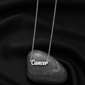 Macro shot of silver-colored Cancer zodiac pendant on black silk and stone background