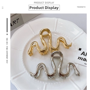 Detail showing snake-shaped hair claws in gold and silver with textured scale patterns