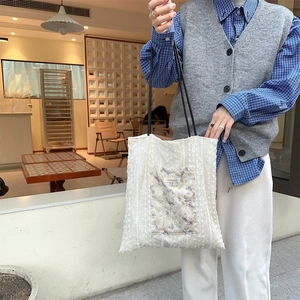 Detail of off-white lace tote bag featuring floral pocket and black leather handles