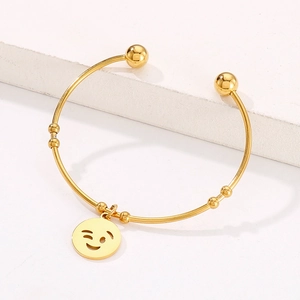 Detail of gold titanium steel open bangle with bead charms and a winking smiley pendant