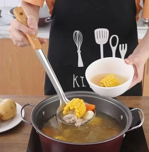 Action shot of stainless steel slotted spoon with wooden handle lifting corn soup from a pot