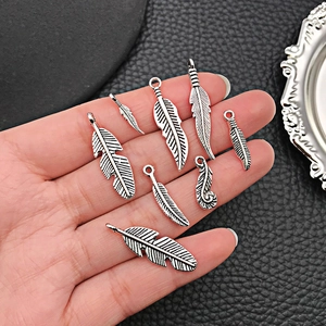 Set of eight vintage silver alloy feather pendants in various sizes on a black background