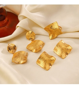 Golden irregular hammered jewelry set including earrings and rings on beige satin