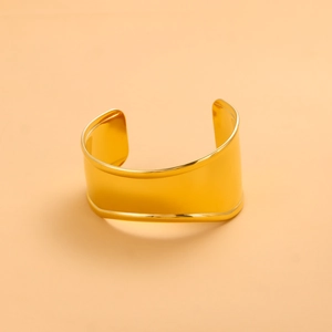 Macro detail of wide gold-plated open bangle with high-polished metallic surface