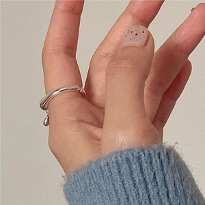 Detail of silver water drop charm ring on finger with soft knit sweater background