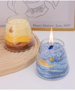 Close-up of dual gradient sand art candles in glass cups with glowing wick flame