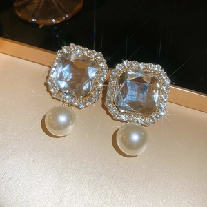 Close-up of vintage square zircon earrings with white pearl pendants in gold finish
