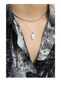 Detail of layered S925 silver necklace with tulip motif and oval shell pendant on model