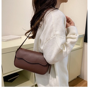 Detail of dark brown leather shoulder bag worn by model in minimalist bright setting