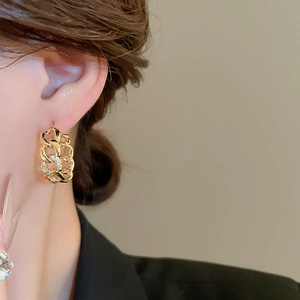 Close-up of a gold plated Cuban link earring with small rhinestones worn by a model