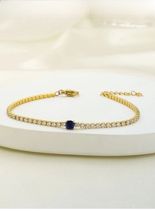 Close-up of titanium steel gold tennis bracelet with blue gem on silk backdrop