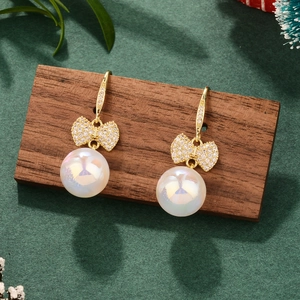 Close-up of pearl bow earrings on wood with festive pine and berry decorations