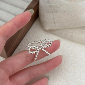 Detail of silver beaded bow ring on finger with soft lighting and elegant jewelry box